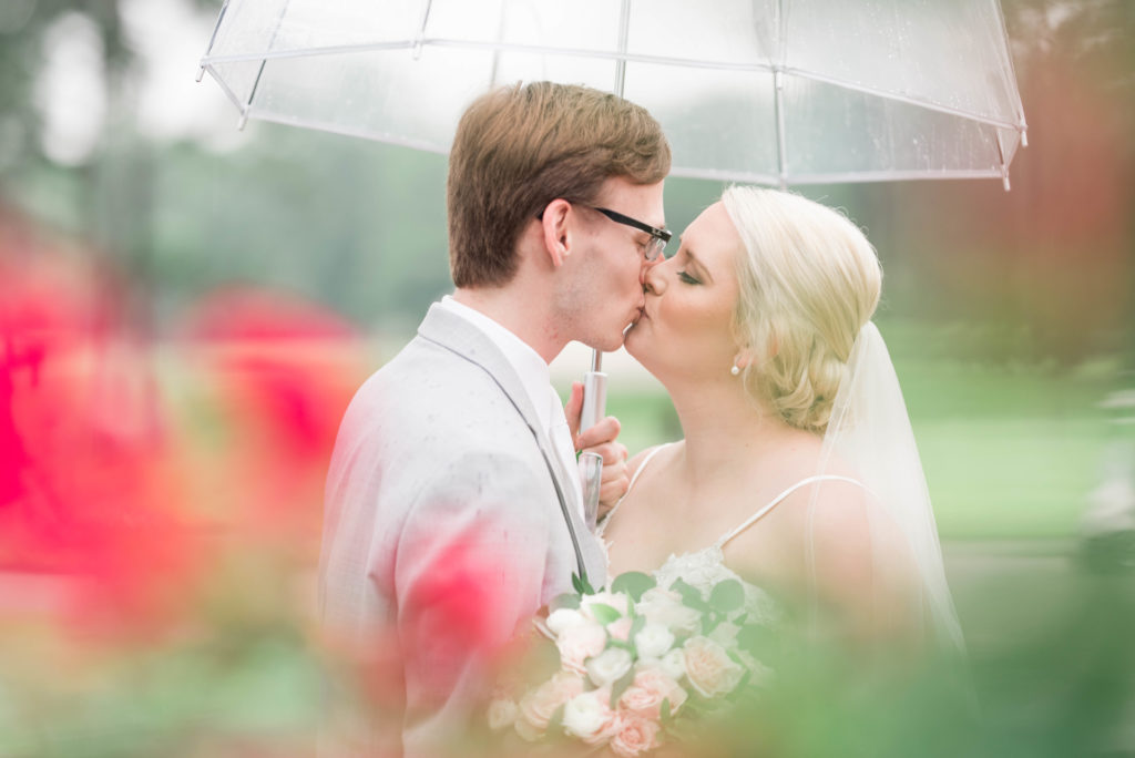 Bride and groom kissing under an umbrella on their rainy wedding day
